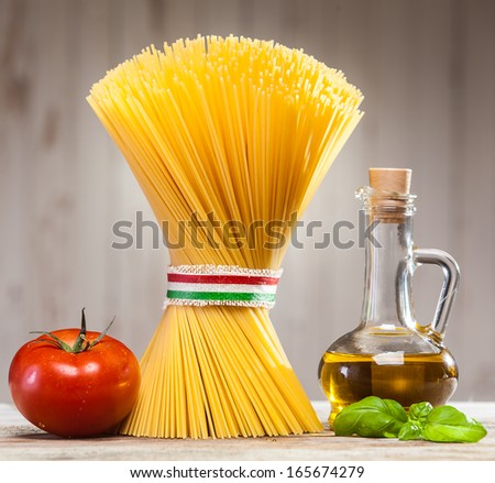Bundle of uncooked dried Italian spaghetti tied with a ribbon in the colours of the national flag - red, white and green - on a kitchen counter with fresh basil leaves, tomato and a jar of olive oil