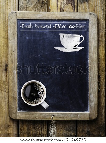 Fresh brewed filter coffee - handwritten on an old vintage school slate used as an advertising sign in a rustic coffee shop with a fresh cup of aromatic coffee in the bottom corner