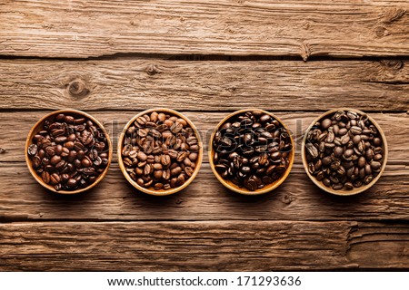 Assorted raw and roasted coffee beans in small individual containers on a rustic, weathered textured driftwood background, overhead view with copyspace