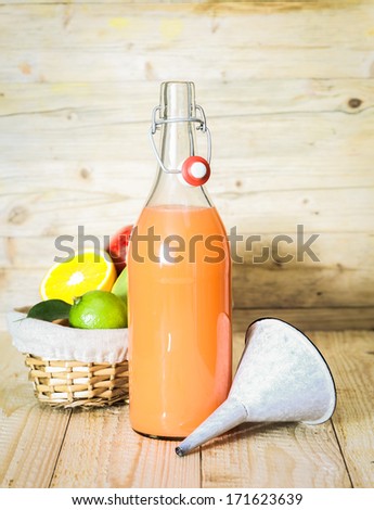 Bottle of homemade fruit juice made from a blend of liquidised mixed citrus fruit with a basket of fresh ingredients and a small metal funnel alongside