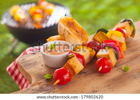 Healthy picnic lunch at a summer barbecue with grilled smoked Tofu and vegetable kebabs served with a savory sauce and toasted baguette on a wooden table