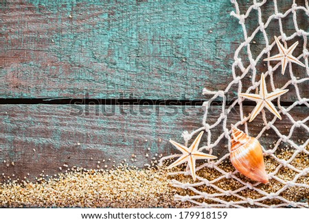 Rustic marine background with copyspace on weathered turquoise blue wooden boards decorated with diamond mesh fish net, starfish and a seashell on a bed of beach sand, mementos from a summer vacation