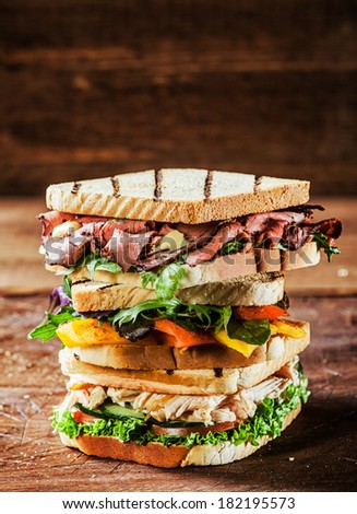 Choice of tasty toasted sandwiches piled on top of each other with shredded chicken breast, rare roast beef and cheese garnished with pepper, herbs and salad ingredients on a rustic table , copyspace