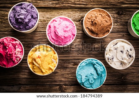 Selection of gourmet flavours of Italian ice cream in vibrant colors served in individual plastic tubs on an old rustic wooden table in an ice cream parlor, overhead view
