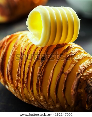 Healthy sliced baked potato cooked with the jacket on in foil and served topped with a creamy butter curl on a dark background, close up view