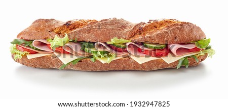 Delicious baguette sandwich with various ripe vegetables and ham slices served on white table in studio