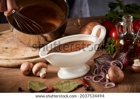 Chef preparing a serving of delicious spicy rich gravy whisking it in a pot with a close up view on a full sauce boat or pitcher in the foreground Foto stock © 