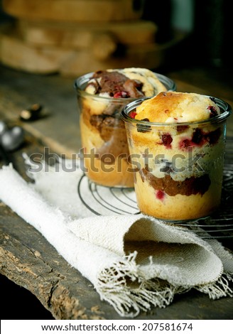 Individual cake desserts in glasses with a fruity variety with berries and a chocolate and vanilla marbled cake cooling on a wire rack on a burlap cloth in a rustic country kitchen