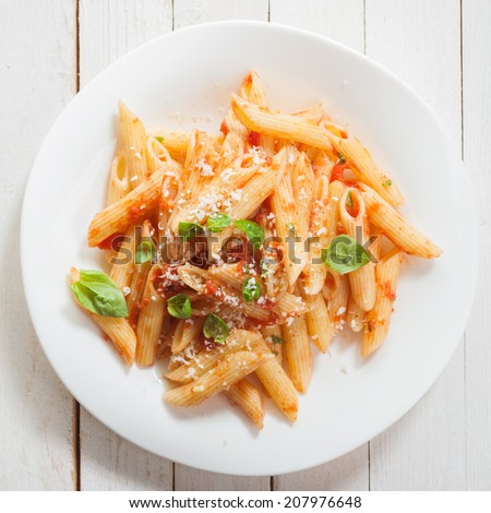 Italian penne pasta or noodles with a savory tomato sauce, fresh basil and grated parmesan cheese viewed close up from above on a white plate in square format