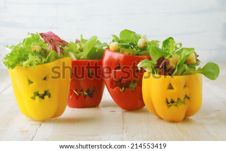 Colorful Halloween food background with colorful healthy stuffed red and yellow sweet bell peppers with cutout faces in the skin like Halloween jack-o-lanterns filled with green salad and cheese