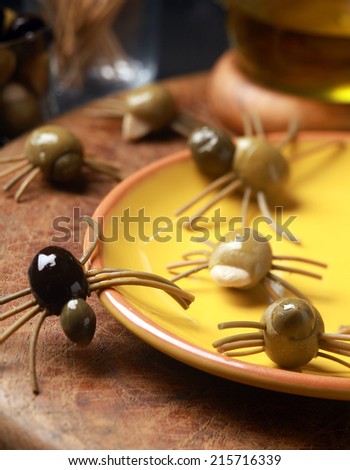 Scary creepy Halloween spider snacks served at a festive party made from cured green and black olives with pasta legs crawling all over the table from a yellow plate