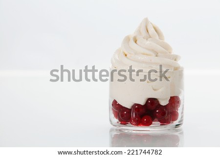 Ripe redcurrants topped with vanilla frozen yogurt served as a party dessert in a glass dish on a white table with copyspace
