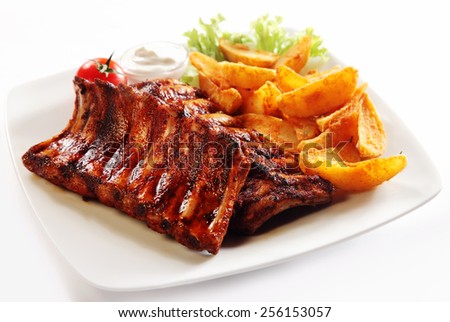 Close up Gourmet Grilled Pork Rib and Fried Potato Wedges on White Plate with Sauce and Veggies, Isolated on White Background.