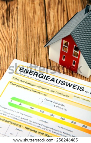 Energy report for a house purchase or sale which rates the efficiency of usage and consumption with a German title alongside a model house on a wooden table
