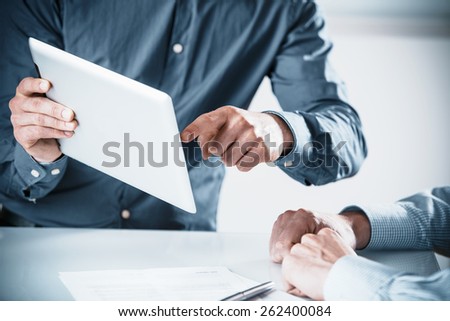 Two businessmen in a meeting discussing a projet on a tablet computer pointing to the screen, close up of their hands