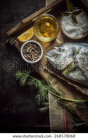 Uncooked whole fresh fish with herbs, olive oil and spices for marinating and rubbing lying on a vintage wooden tray in a rustic country kitchen, overhead view with copyspace