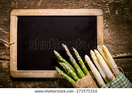 Small Blank Black Chalkboard with Fresh Asparagus on the Corner, Placed on Top of Rustic Wooden Table, Emphasizing Copy Space.