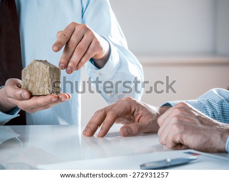 Close Up of Businessman Holding Small Rustic House Model in Meeting with Co-Workers in Real Estate Concept Image