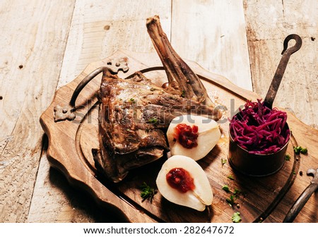 Angled View of Roasted Venison Haunch on Wooden Tray with Prepared Pears on Rustic Table with Evergreen Sprigs and Deer Antlers