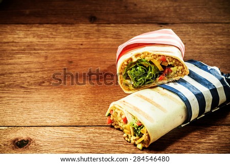 Two Cut Halves of Healthy Vegetarian Couscous Filled Grilled Burrito Wraps in Striped Wrappers Stacked on Wooden Surface