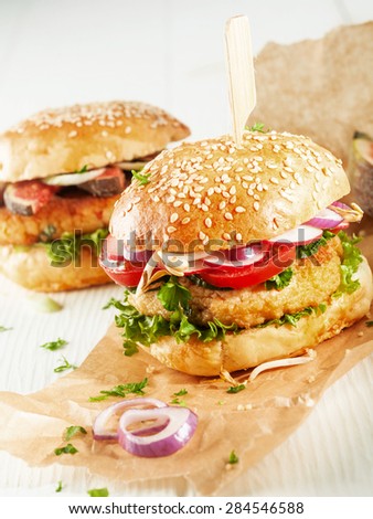Two Vegetarian Couscous Burgers with Fresh Toppings and Herbs on Sesame Seed Rolls with Onion Slices on Brown Paper Wrapper
