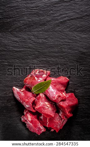 Cervine wild deer venison trimmed and diced standing ready for cooking in a tasty venison goulash on a textured black background with copyspace, overhead view
