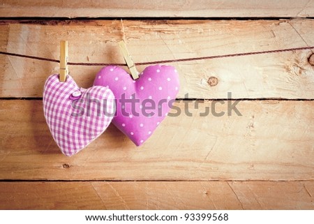 Two pretty pink material Valentine hearts hanging on a line with clothes pags over wooden boards.