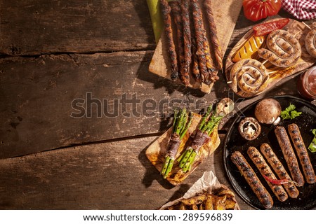 Assorted grilled food including sausages, potato wedges and asparagus bacon wraps from a summer barbecue on a rustic wooden picnic table with copyspace