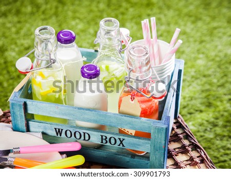 Assorted beverages standing open in a wooden box ready for a summer picnic with fruit juices, lemonade and farm fresh milk on a green lawn outdoors