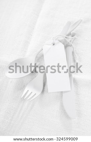 Pure white - a monochromatic all white concept for food or catering with white utensils tied with a blank white gift tag over a textured white tablecloth with copyspace