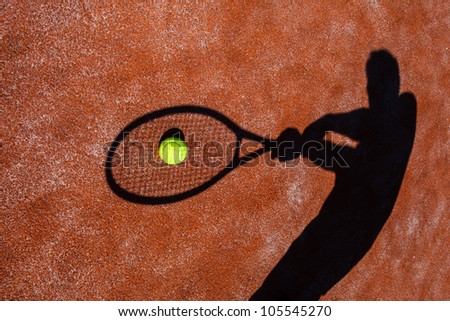 shadow of a tennis player in action on a tennis court (conceptual image with a tennis ball lying on the court and the shadow of the player positioned in a way he seems to be playing it)
