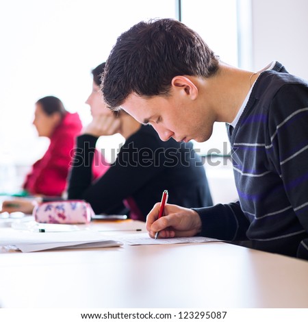 young, handsome male college student sitting in a classroom full of students during class (color toned image; shallow DOF)