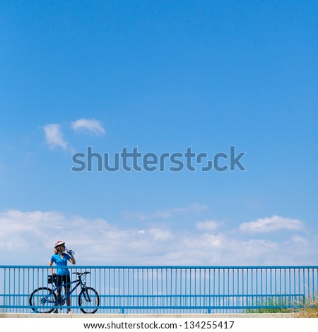 Background for poster or advertisment pertaining to cycling/sport/outdoor activities - female cyclist during a halt on a bridge against blue sky (color toned image)