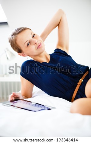 Pretty, young woman using her tablet computer in bed, after coming home from work (shallow DOF; color toned image)