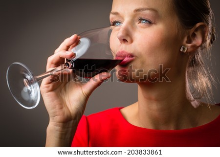 Elegant young woman in a red dress, having a glass of red wine