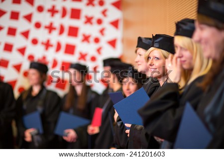 Pretty female college graduate at graduation with classmates, holding their degres. looking happy about their accomplishment