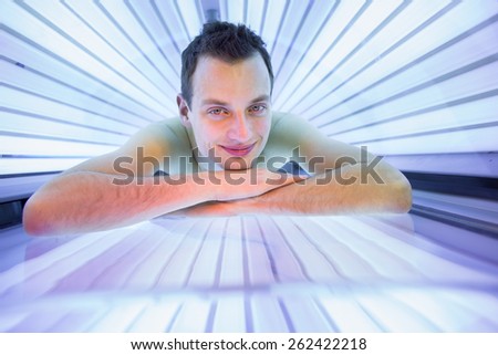 Handsome young man relaxing during a tanning session in a modern solarium, taking care of himself, enjoying the artificial sunlight.