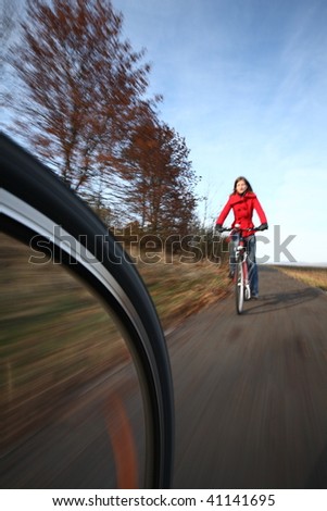 Biking (the image is motion blurred to convey movement; focus is on the wheel, the female biker is left out of focus)