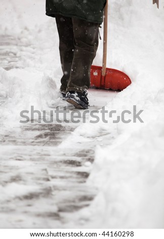Man shoveling snow from the sidewalk in front of his house after a heavy snowfall in a city