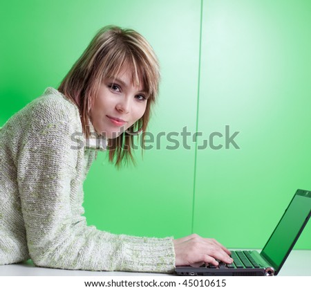pretty young college student working on her laptop computer in front of a green wall (looking at you)