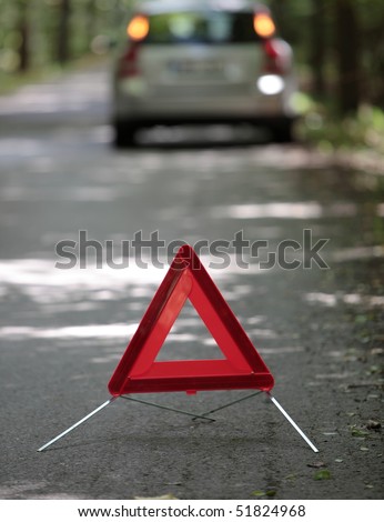 broken down car with warning triangle behind it waiting for assistance to arrive (shallow depth of field, the focus is on the triangle, the car is left out of focus)