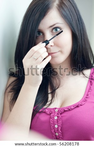 pretty young woman applying mascara /eye shadows in front of a mirror (color toned image)