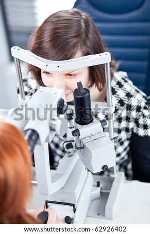 optometry concept - pretty young woman having her eyes examined by an eye doctor (color toned image)