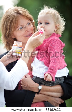 cute little girl outdoors in a park being fed apple pur?e by her mom and held by her grandmother (shallow DOF, selective focus)