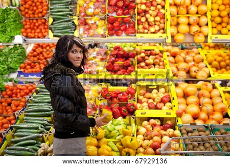 Beautiful young woman buying fruits and vegetables at a produce department of a supermarket/grocery store