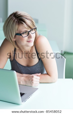 Portrait of a young woman pensively looking out of the window while sitting in front of her laptop
