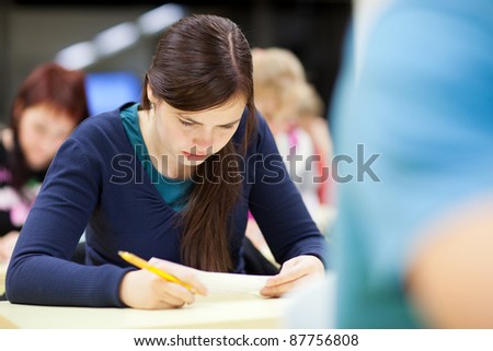 pretty, female college student sitting in a classroom full of students during class (shallow DOF; color toned image)