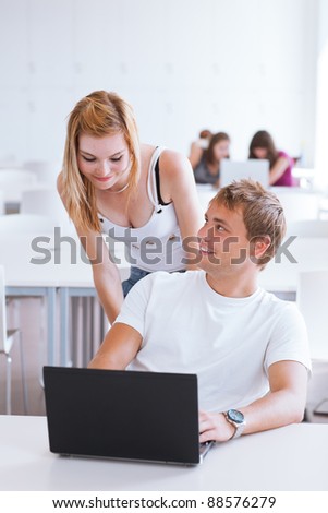 two college students having fun studying together, using a computer in a university library/study room (shallow DOF, color toned image)