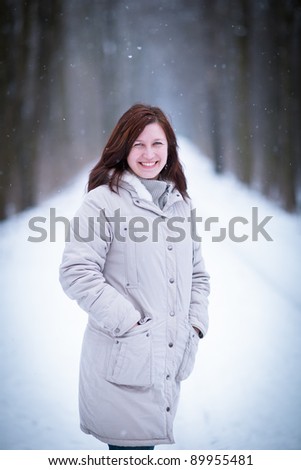 Enjoying the first snow: young woman outdoors on a lovely forest path watching the snowflakes falling (color toned image)