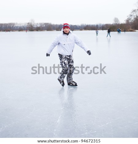 Handsome young man ice skating outdoors on a pond on a cloudy winter day (color toned image; shallow DOF)